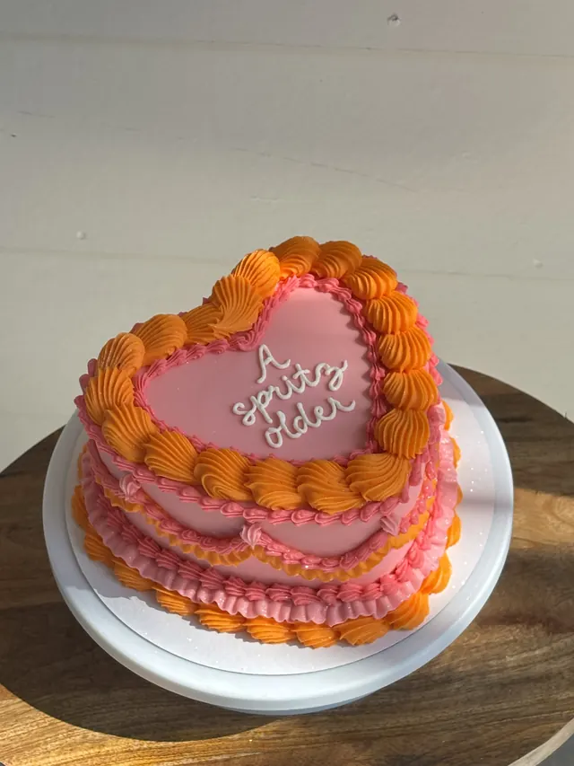 Pink heart cake with orange piping and "A spritz older."